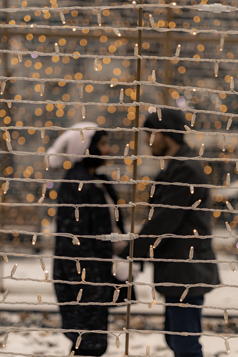 A couple kissing behind a curtain of string lights